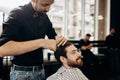 Mustachioed barber dressed in a black shirt with a red bow tie makes a stylish hairstyle to young man in a barbershop