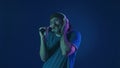 A mustachioed man in white wireless headphones dances and sings into a microphone. Woman in studio on blue background Royalty Free Stock Photo