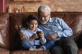 Happy little grandkid sit on sofa use cellphone with grandfather Royalty Free Stock Photo