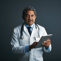 My digital doctoring assistant. Studio shot of a mature doctor using a digital tablet against a gray background.