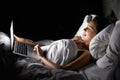 My new snuggle buddy. An attractive woman using her laptop while lying in bed at home. Royalty Free Stock Photo