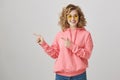 My place is right behind corner. Positive attractive young caucasian female with curly hair in stylish eyewear pointing