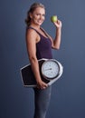 This is my secret. Studio portrait of an attractive mature woman holding an apple and a weightscale against a blue Royalty Free Stock Photo