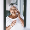 My skin looks so radiant with this on. a cheerful mature woman applying skin cream on her face while looking into a Royalty Free Stock Photo