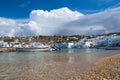 Mykonos, Greece - May 04, 2010: sea beach with boats on cloudy blue sky. Houses on mountain landscape by sea