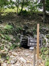 A mysterious cave entrance leading underground with a sign beside it that warns to not enter in spanish and english. Royalty Free Stock Photo