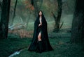 Mysterious fantasy gothic woman dark witch obsessed by evil. Girl demon vampire in black dress cape hood. walk in dark Royalty Free Stock Photo