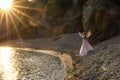 A mysterious female silhouette with long braids stands on the sea beach with mountain views, Sunset rays shine on a