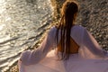 A mysterious female silhouette with long braids stands on the sea beach with mountain views, Sunset rays shine on a