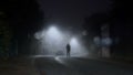 A mysterious figure standing in the middle of a road with street lights on a misty winters night. With a blurred, bokeh, out of Royalty Free Stock Photo