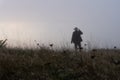 A mysterious figure wearing a fedora hat, standing out of focus in a field in the background on a misty winters day