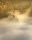 Mysterious fog rising over a valley with a colorful autumn forest at sunrise Royalty Free Stock Photo