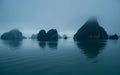 Mysterious gloomy shot of rock hills in the sea covered in fog in Halong Bay, Vietnam