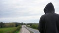 A mysterious hooded figure, back to camera. Looking down on an empty motorway in the countryside. With copy space Royalty Free Stock Photo