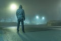 A mysterious hooded figure with back to camera, standing on a road in a light industrial urban area. On a moody, foggy, winters Royalty Free Stock Photo