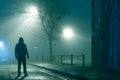 A mysterious hooded figure holding a phone, standing in a city street. On a moody foggy winters night Royalty Free Stock Photo