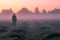 A mysterious hooded, figure standing in a field on a beautiful early misty morning, looking at the sunrise