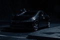 A mysterious hooded figure, standing next to a car with the door open. Looking into the car, underneath a street light at night