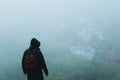 A mysterious hooded hiker with rucksack, looking downfrom a hill on a town. On a foogy, rainy summers day