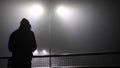 A mysterious, lonely hooded figure, back to camera. Standing on a bridge, over looking a motorway on a misty winters at night Royalty Free Stock Photo