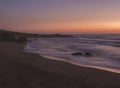 Mysterious long exposure view of sand beach Praia Grande de Almograve with blurred ocean waves in pink orange and purple