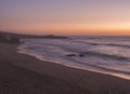 Mysterious long exposure view of sand beach Praia Grande de Almograve with blurred ocean waves in pink orange and purple