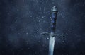 mysterious and magical photo of silver sword over gothic snowy black background. Medieval period concept. Royalty Free Stock Photo