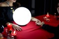 Mysterious magnificent beautiful woman fortune teller in black dress with magical crystal ball looking at customer palm, reading Royalty Free Stock Photo