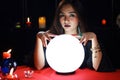 Mysterious magnificent beautiful woman fortune teller in black dress reading future on luminous crystal ball, dark witch casting a Royalty Free Stock Photo