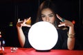 Mysterious magnificent beautiful woman fortune teller in black dress reading future on luminous crystal ball, dark witch casting a Royalty Free Stock Photo