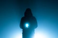 A mysterious moody hooded figure, holding a magical glowing light silhouetted against back ,light on a foggy atmospheric winters Royalty Free Stock Photo