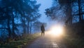 A mysterious moody photo of a a man silhouetted against car headlights on a forest road on a foggy winter evening