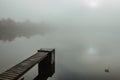 Mysterious morning by lake. Foggy autumn mystery atmosphere. Wooden pier on the pond.Magic mood. Misty fall day. Speechless place