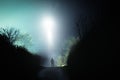 A mysterious scary UFO above a hooded figure. On a spooky country road. On a foggy winters night