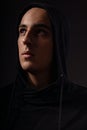 Mysterious serious man in black hoodie with hood on the head looking up on dark background. Dangerous criminal person Royalty Free Stock Photo