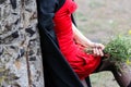 Mysterious sexy blonde woman in a red dress and black cloak, with a black veil on her head. in nature next to an old, almost