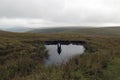 A mysterious silhouette of a man reflected in water with no one above on a bleak moorland hillside