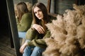 Mysterious smiling young girl in dark green knitted cozy sweater sitting on the floor. Studio conceptual photo