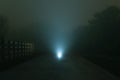 A mysterious spooky glowing light on a road, with a shallow depth of field. On a moody, foggy, atmospheric winters night