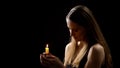 Mysterious woman holding candle in hands and praying with closed eyes, rituals