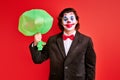 mysterious young caucasian magician holding inflated balloon in hands over red background