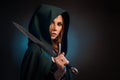 Mysterious young woman keeping sharp knife, wearing green cape with a hood.