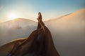 Mystery arabic woman in black long dress stands in desert long train silk fabric fly flytter in wind motion. clothes