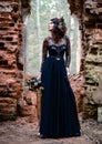 A mystical model in a black dress under an arch against the background of ruins. Black magic, Gothic beauty, halloween, black