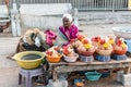An elderly Indian woman selling coconuts and pooja items outside the ancient Hindu temple