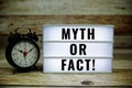 Myth or Fact! text on LED lightbox with alarm clock on wooden background Royalty Free Stock Photo