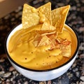 Nachos with cheese sauce in a bowl on a black background