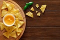 Nachos laid they lie on round wooden stand, cheese sauce, basil, on brown plank dark background, top view, space to copy text Royalty Free Stock Photo