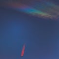 Nacreous cloud and a plane with vapor trails illuminated in red