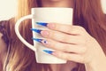 Nail Polish. Modern style new trend blue stilletto Nail Polish. Beauty hands holding white cup with hot beverage tea coffee. Royalty Free Stock Photo